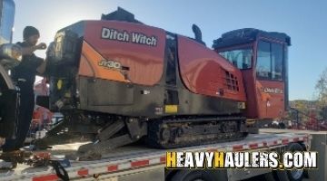 Strapping a Ditch Witch directional drill on a trailer for transport.