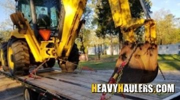 Strapping a New Holland backhoe on a trailer for transport.