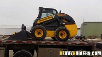 Skid steer transported on a flatbed trailer.